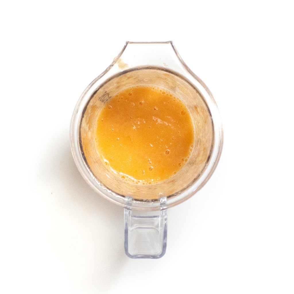 A clear blender with puréed cantelope against a white background.