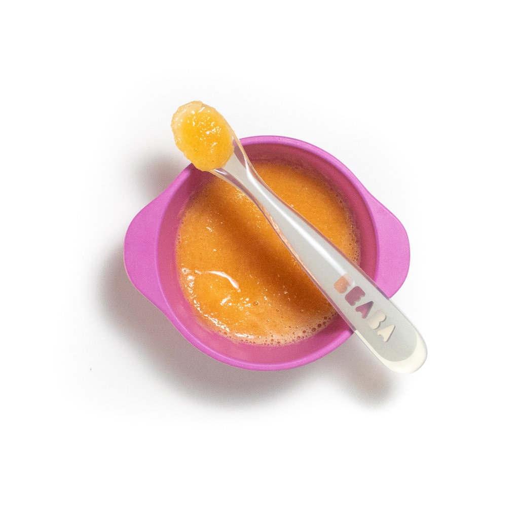 A pink baby bowl with puréed cantaloupe with a spoon resting on top.