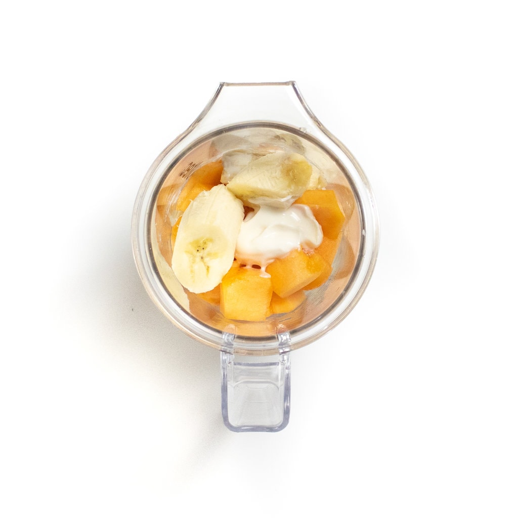 A clear blender with cantaloupe, yogurt and bananas.