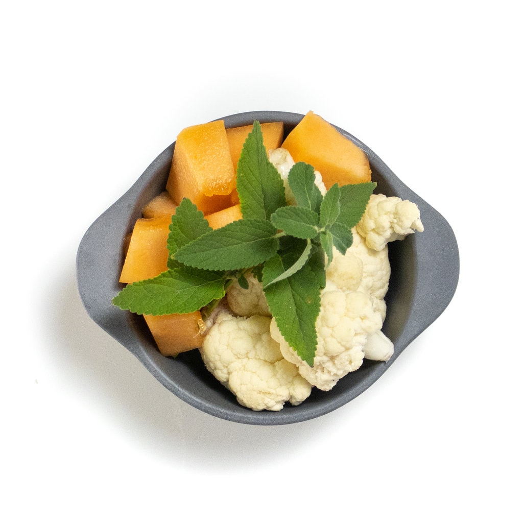 A gray baby bowl with chunks of cantaloupe, mint and cauliflower.