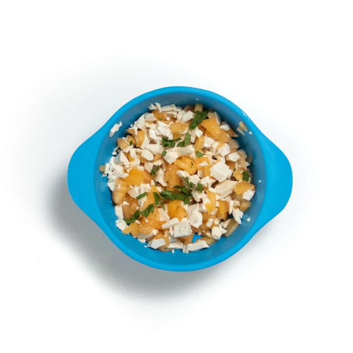 A blue baby bowl with chunks of cantaloupe and tofu with ribbons of mint.