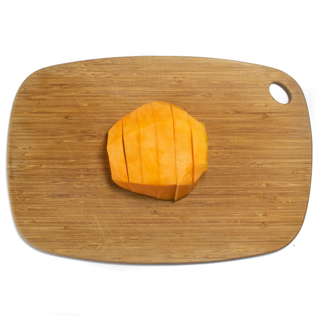 Fix slices of cantaloupe on a wooden cutting board against away backdrop.
