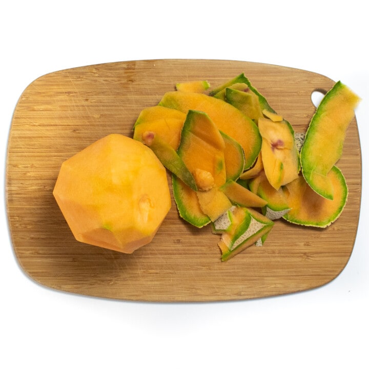 A wooden cutting board with a peeled Cantelope in the skin.