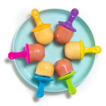 A teal kids plate with a wheel of colorful popsicle sticks and cantaloupe and strawberry cantaloupe popsicles.