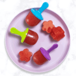 purple kids plate with 3 small watermelon popsicles and a few fun cut out shapes of watermelon. The plate is sitting on my white marble kitchen table.