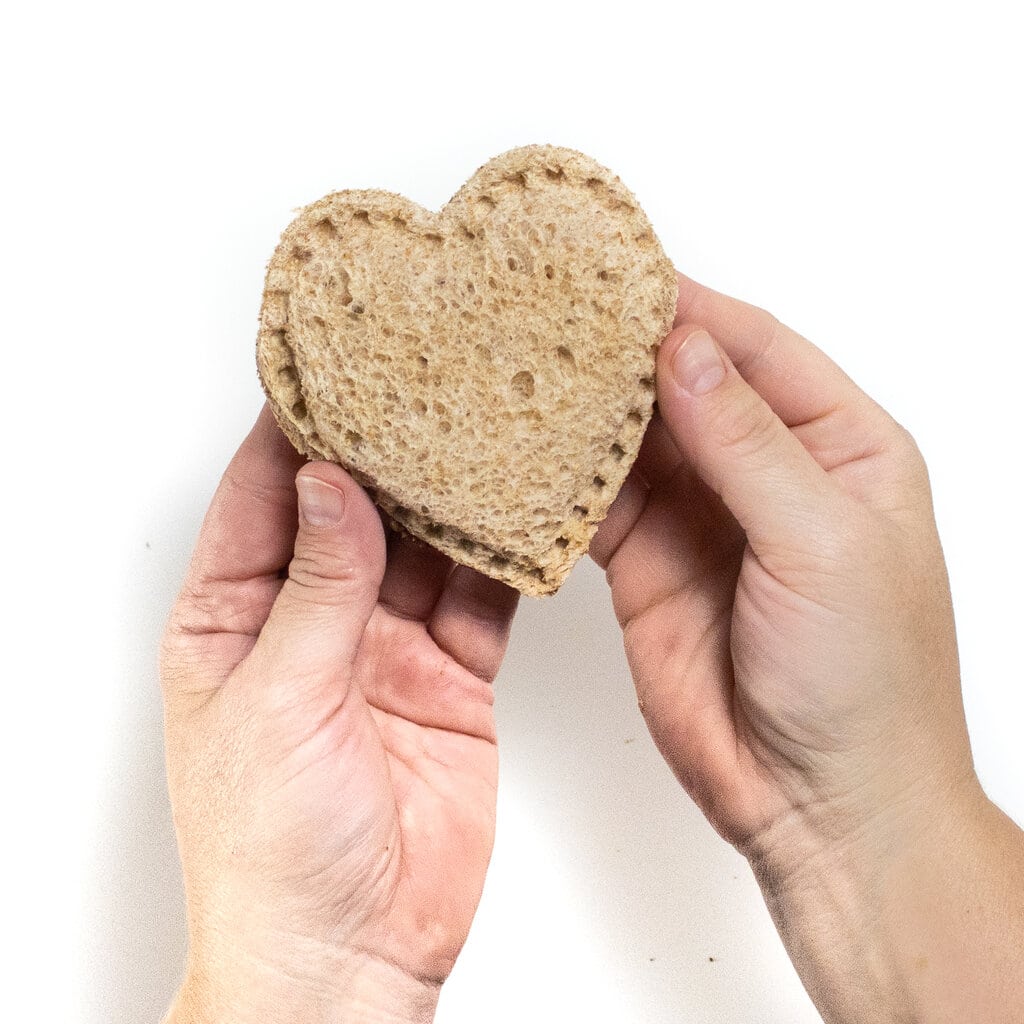 2 hands holding a heart shape uncrustable sandwich against a white background.