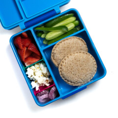 A blue lunchbox filled with two uncrustables sandwiches, cucumbers, strawberries, popcorn and gummy snacks.