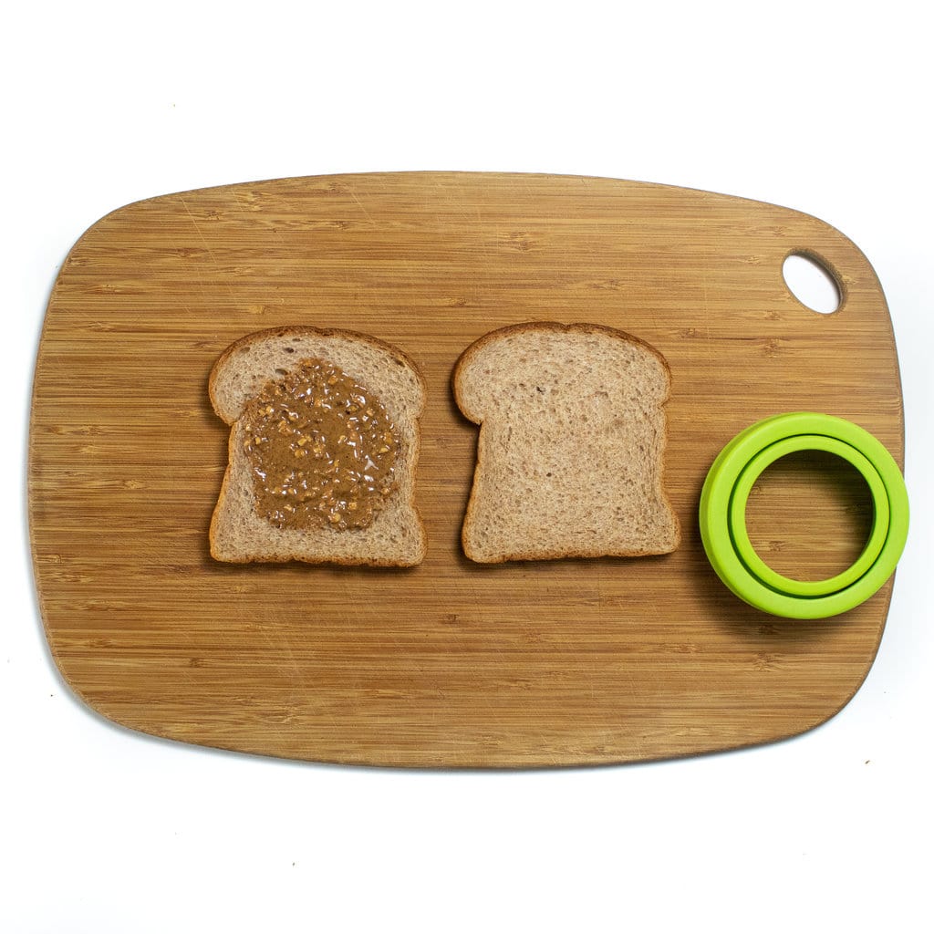 A cutting board with two pieces of bread and an uncrustable cutter.
