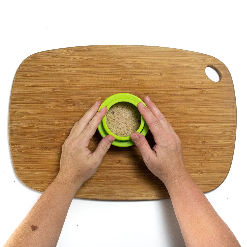 Two hands cutting out a circle shape with a sandwich cutter.