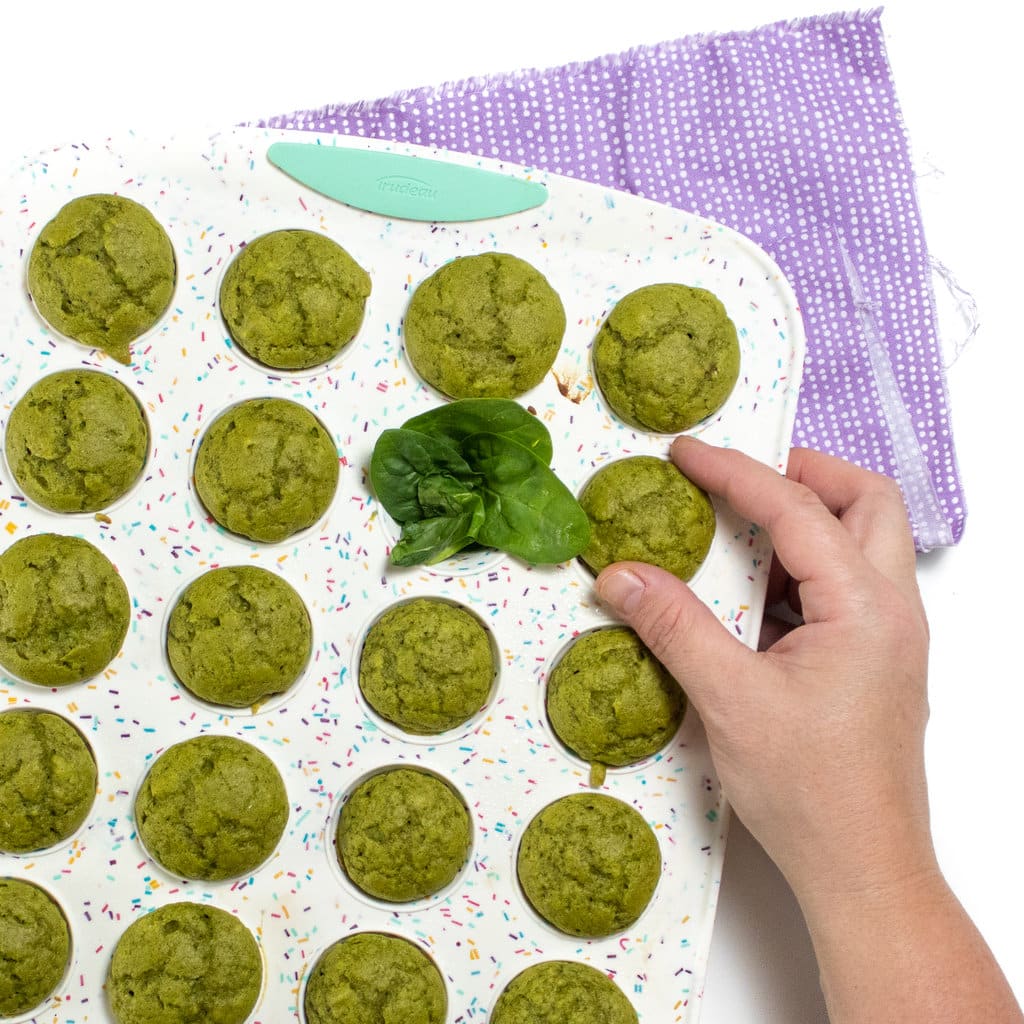 A hand putting a spinach muffin out of a colorful muffin tin.