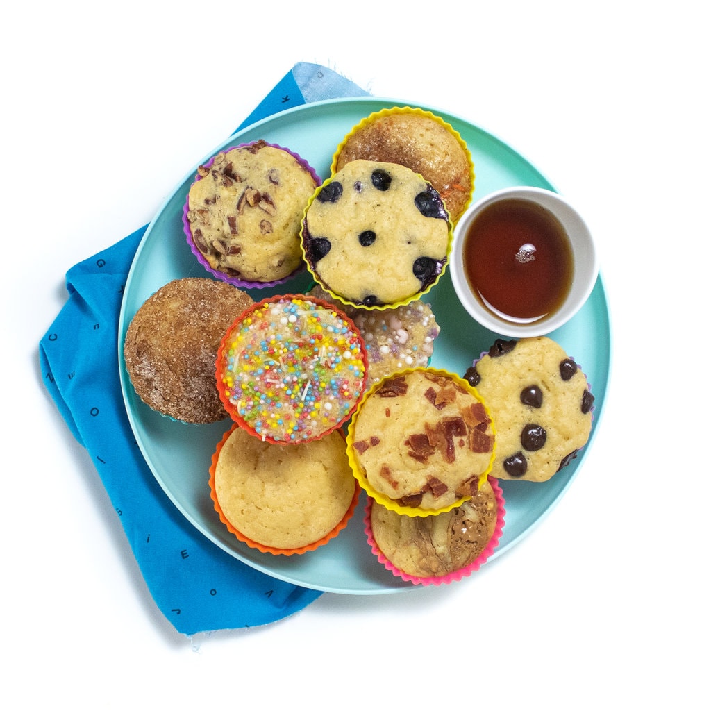 A blue kids play with the blued kids napkin, the plate has pancake muffins with various toppings.
