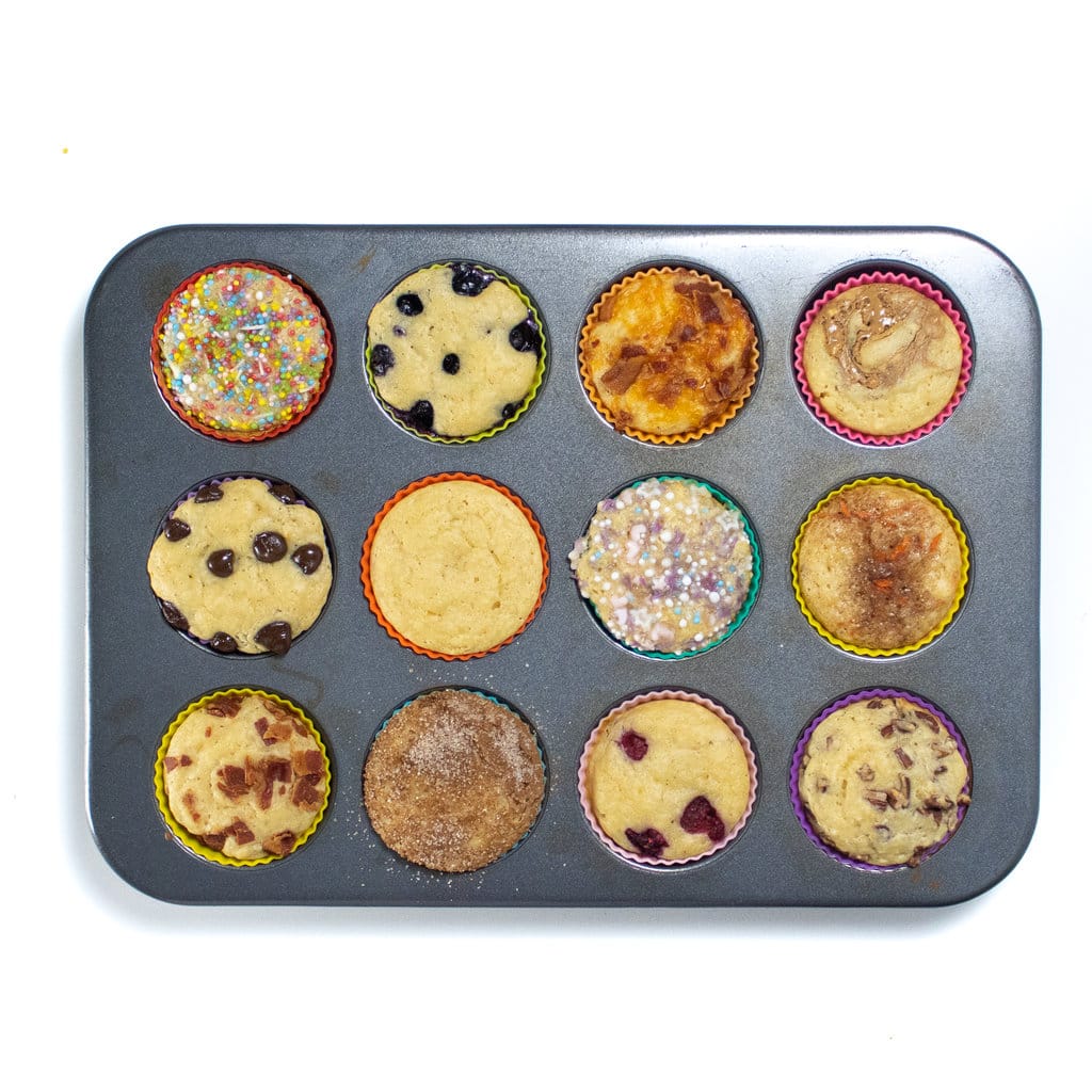 A muffin tin with colorful liners and 12 different pancake muffins baked and ready to eat.