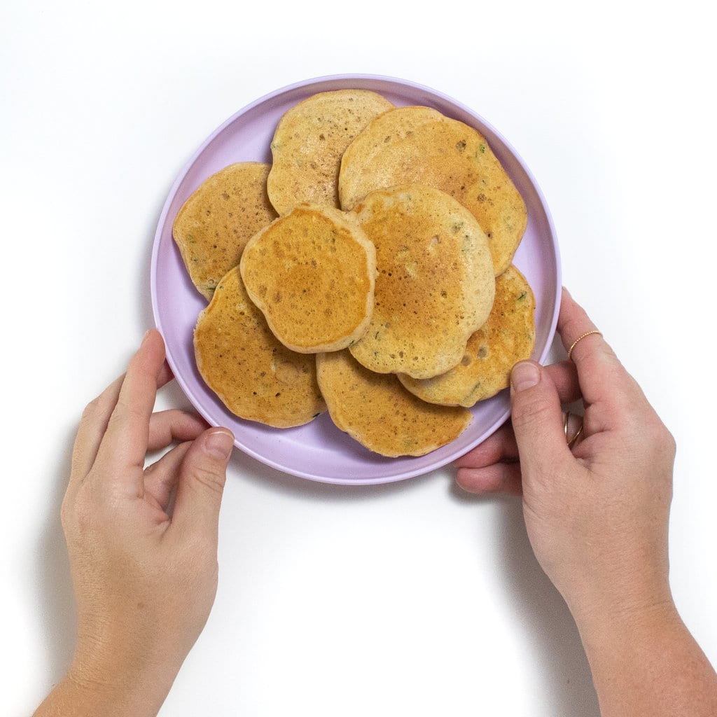 Hands holding a purple kids plate full of zucchini pancakes.