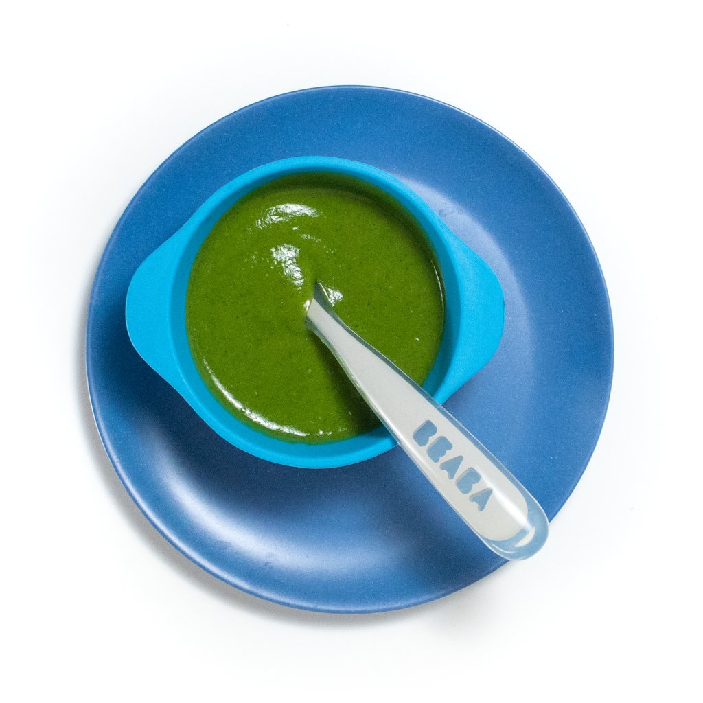 A blue kids plate with a blue baby bowl with zucchini purée with a baby spoon sitting inside.