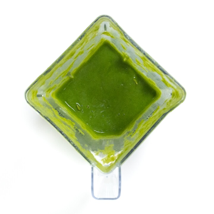 It clear blender against a white background with a bright green zucchini purée for baby.