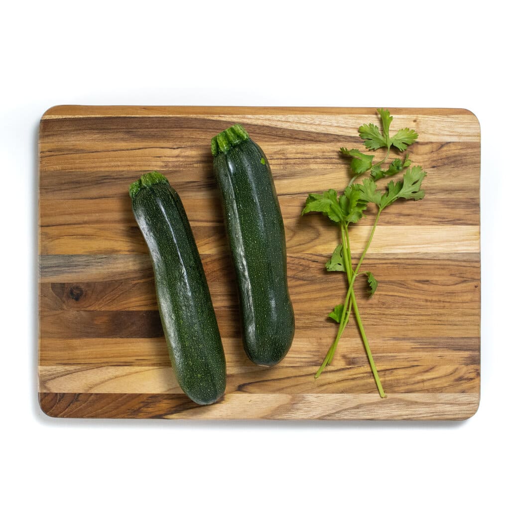 A a wooden cutting board with two zucchini and cilantro.