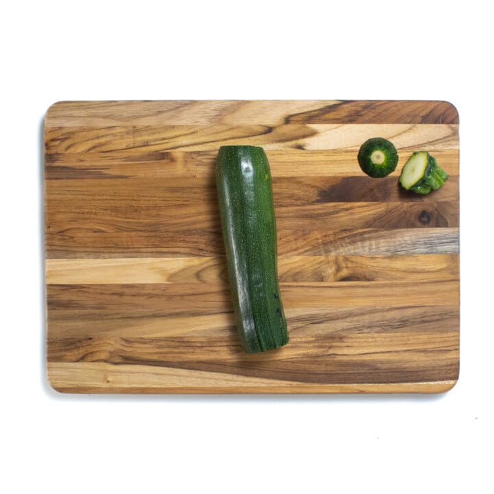 A wooden cutting board with the top and bottom cut off of the zucchini.