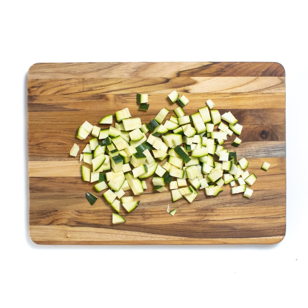A wooden cutting board with small pieces of zucchini cut perfect.