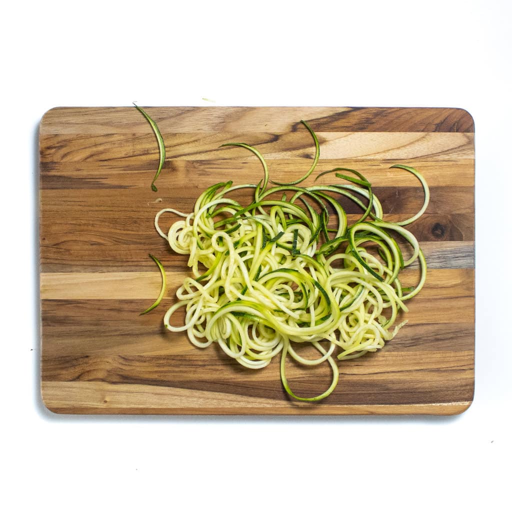 A pile is zucchini noodles on top of a wooden cutting board.