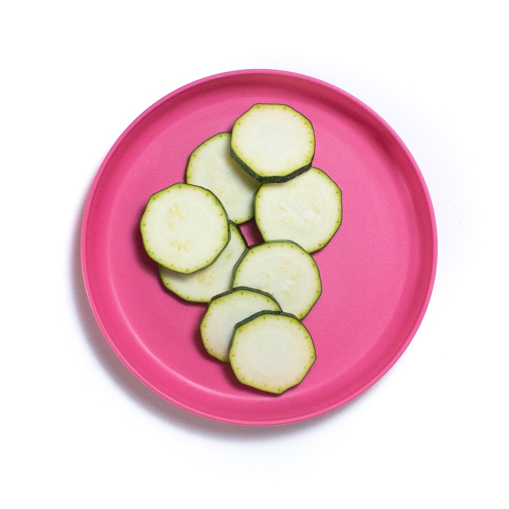 A bright pink kids plate with slices of zucchini.