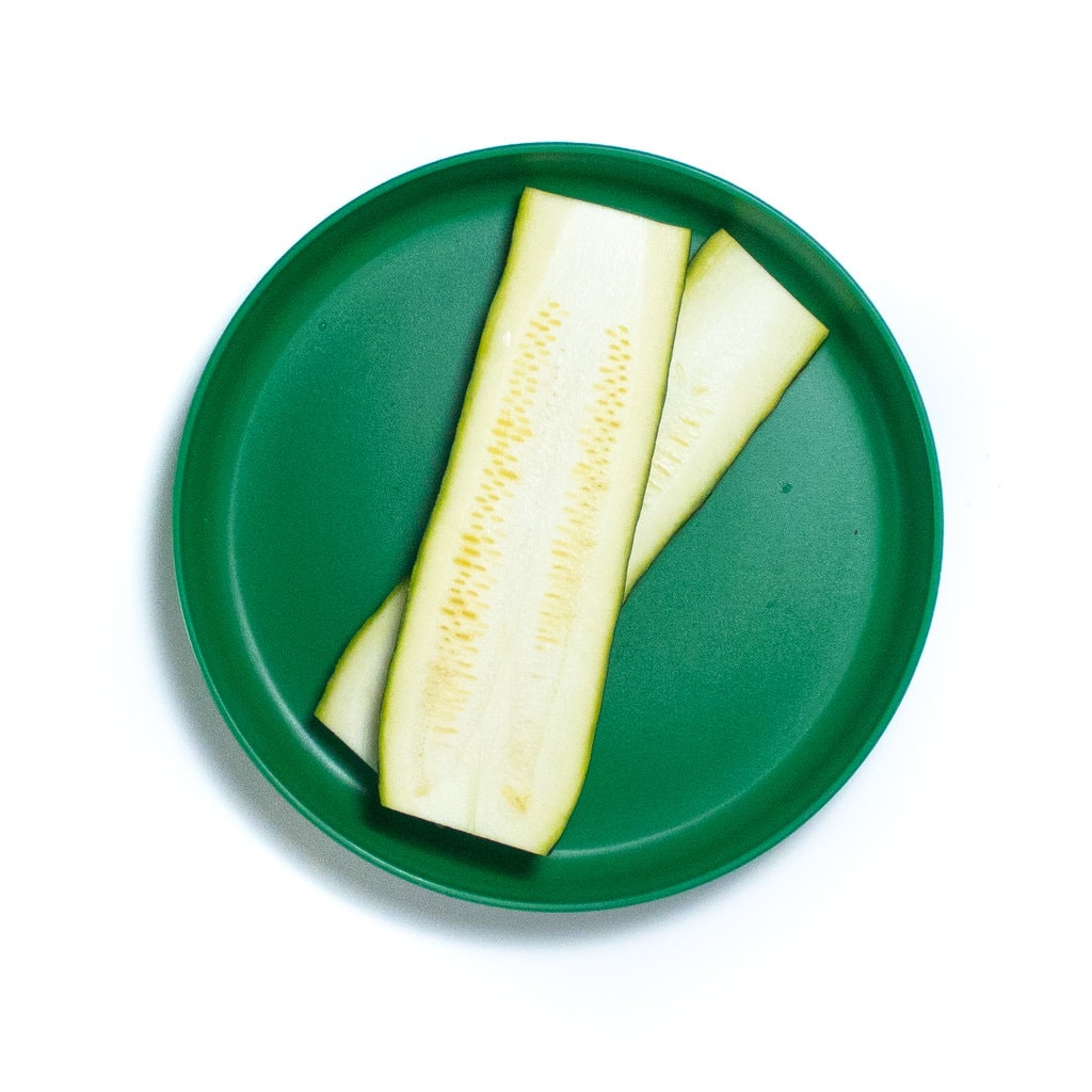 A bright green kids plate with planks of zucchini.
