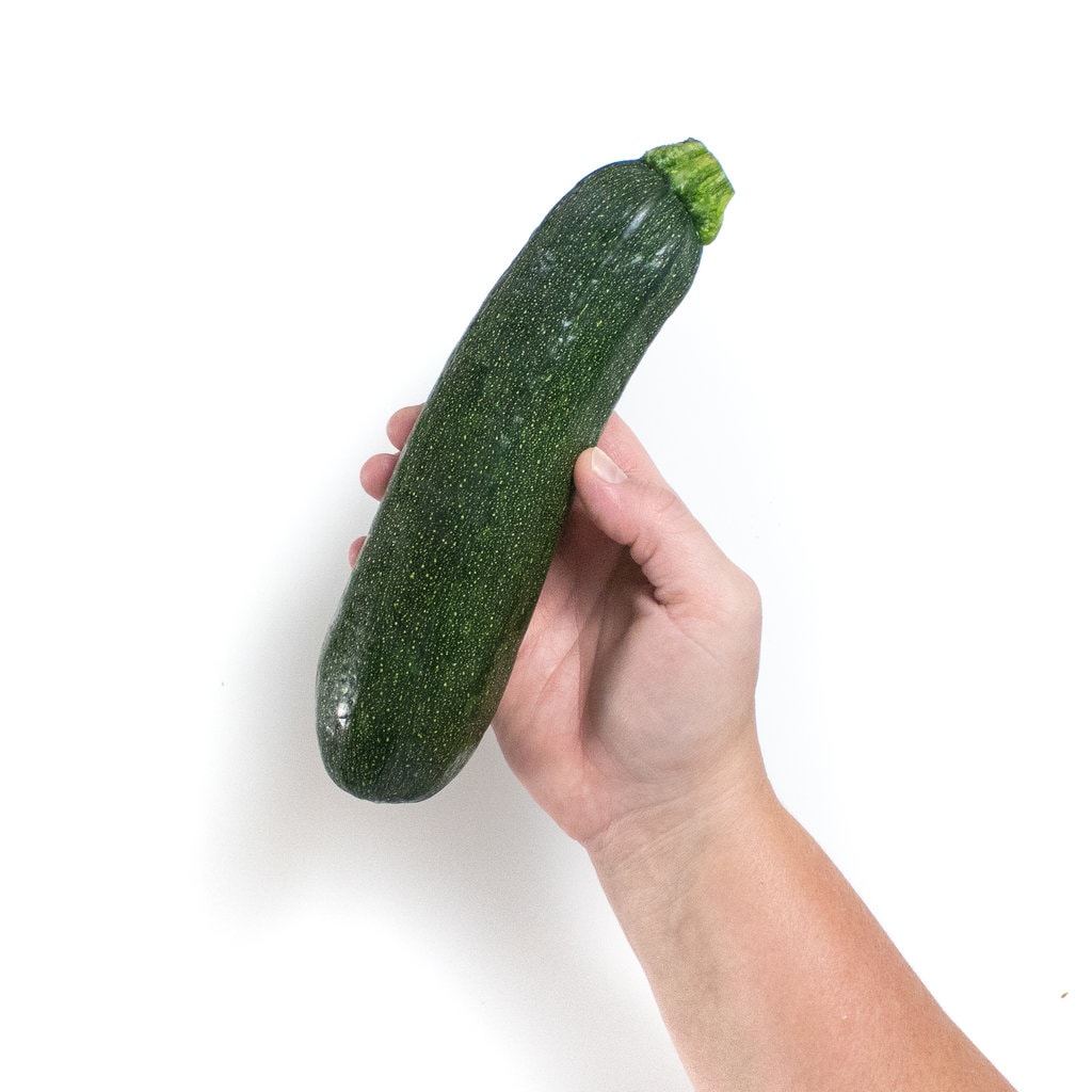 A hand holding a zucchini against a white background.