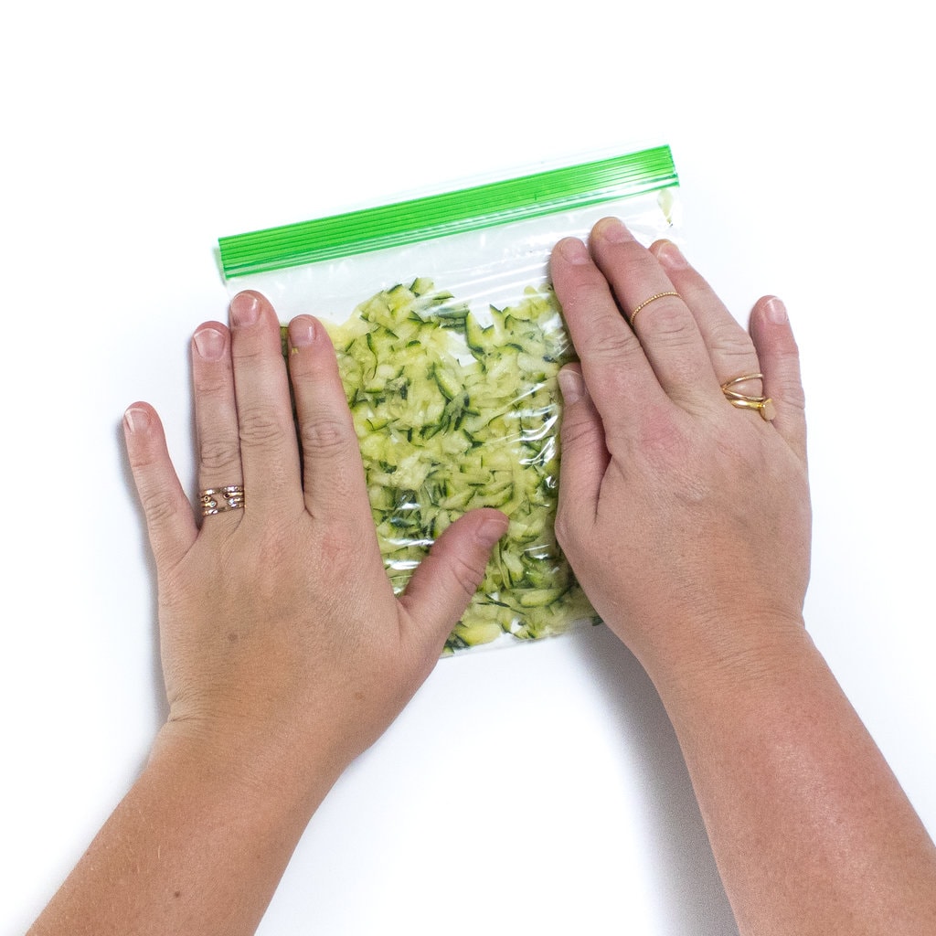 Two hands pressing the air out of a baggie full of grated zucchini.