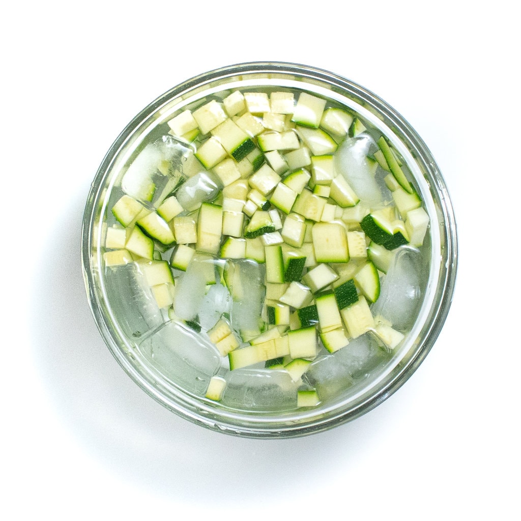 Diced zucchini in a clear bowl with ice water.
