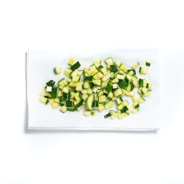diced zucchini sitting on a paper towel against a white background.