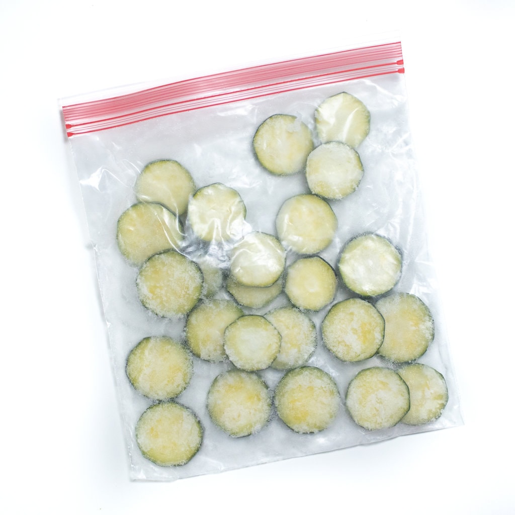 Frozen zucchini slices in a Ziploc bag against a white background.