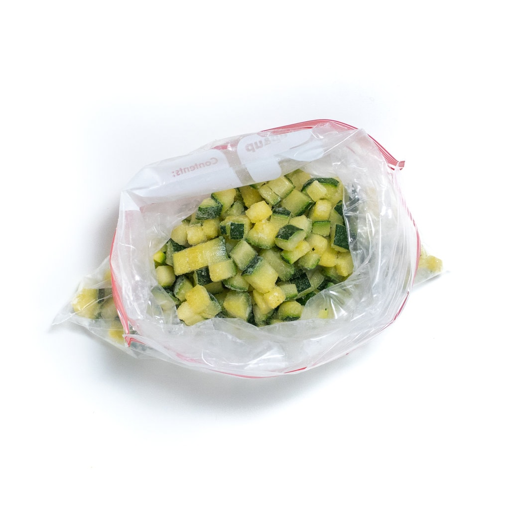 A top view of diced zucchini frozen in a Ziploc bag.