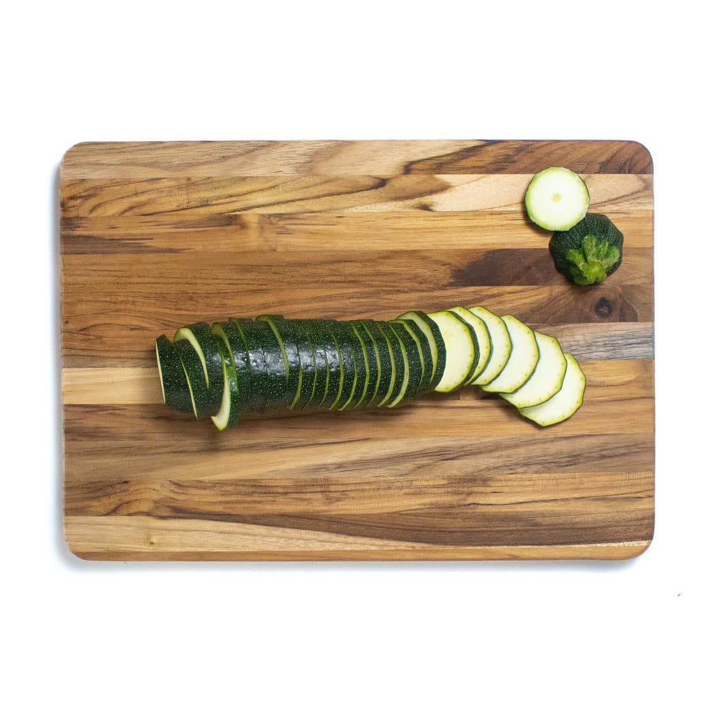 Hey wooden cutting board with an entire zucchini cut into slices.