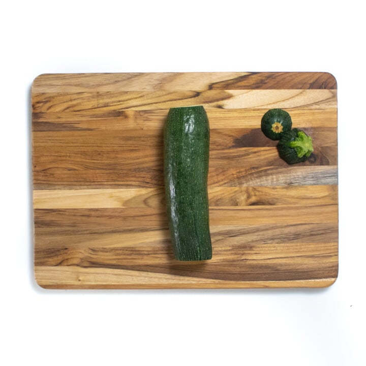 A wooden cutting board with the top and bottom cut off of the zucchini.