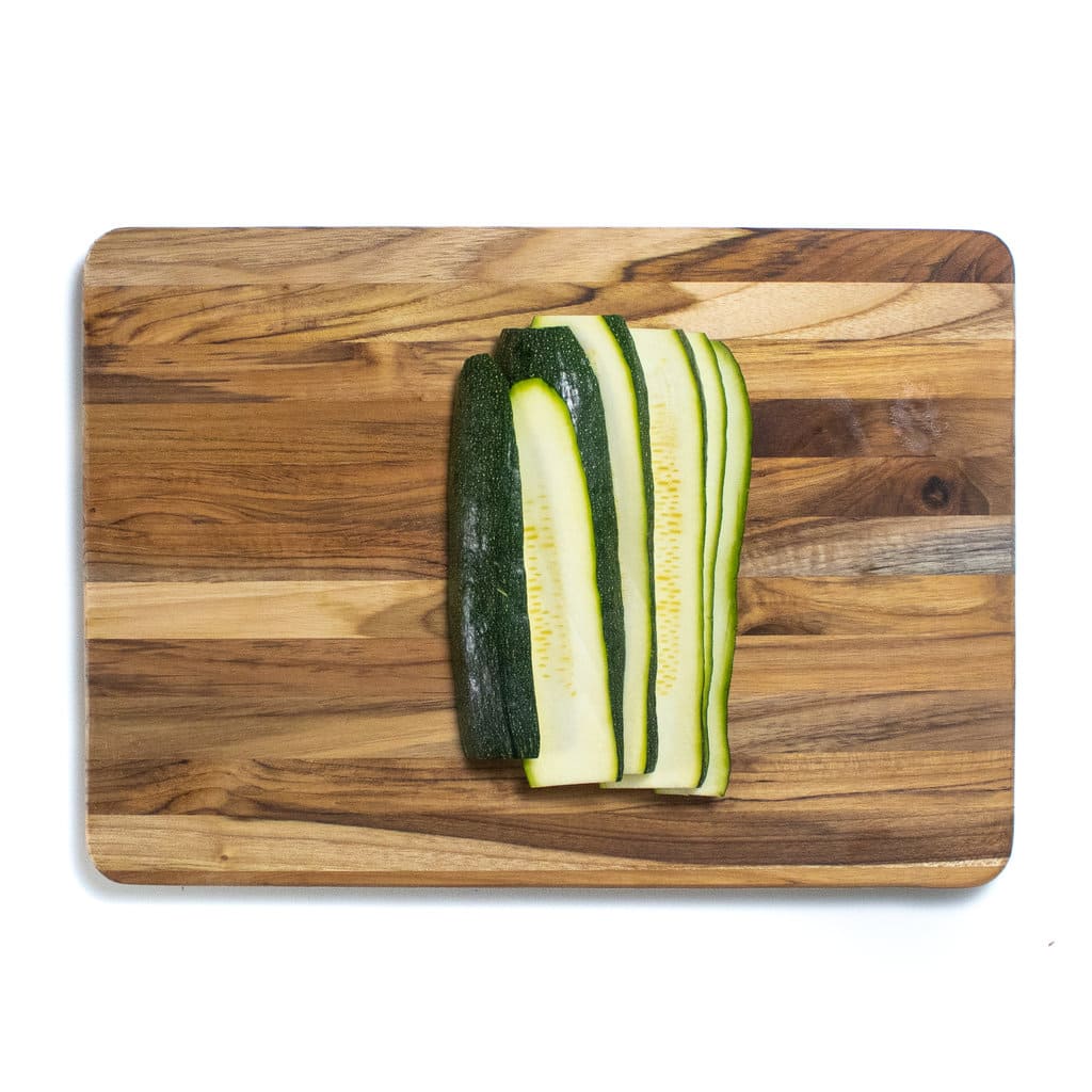 A wooden cutting board with a zucchini cut into planks.