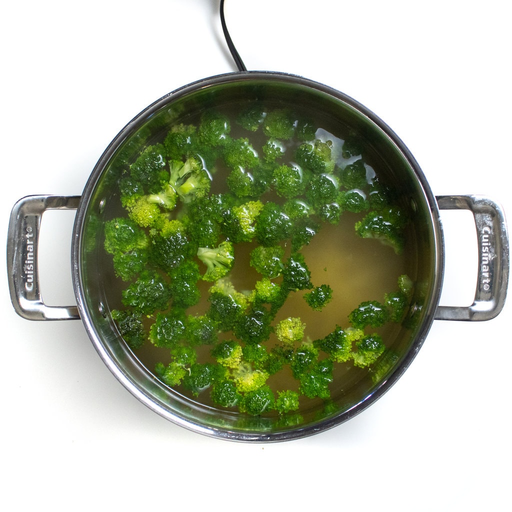 A large silver pot with boiling water with pasta and broccoli in it.