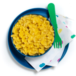 A blue kids plate and bowl filled with butternut squash mac & cheese with a colorful napkin and a green fork.