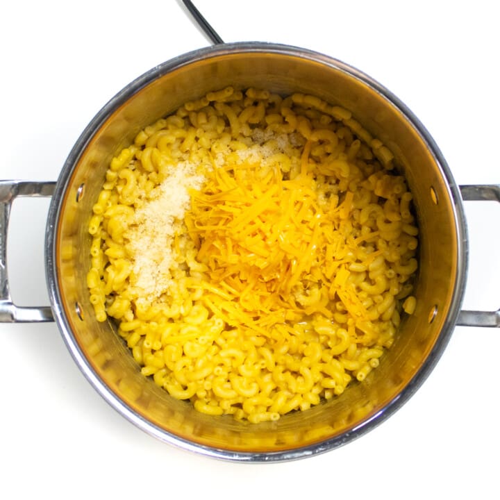 A large silver stock pot full of cooked macaroni with shredded cheese and Parmesan on top.