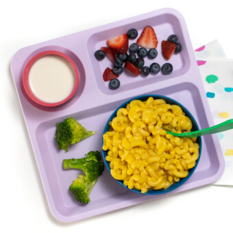 A purple kids school tray for lunch filled with a blue bowl full of butternut squash mac & cheese, broccoli, berries in milk.