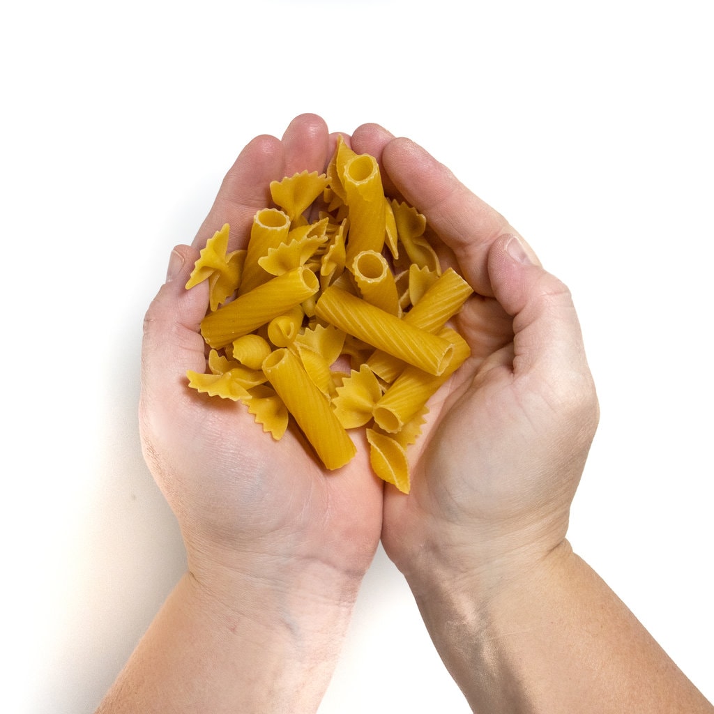 Hands holding several different types of dry pasta. 