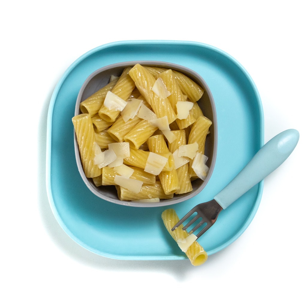 Gray baby bowl sitting on a blue baby plate with tube pasta and flakes of cheese on top.