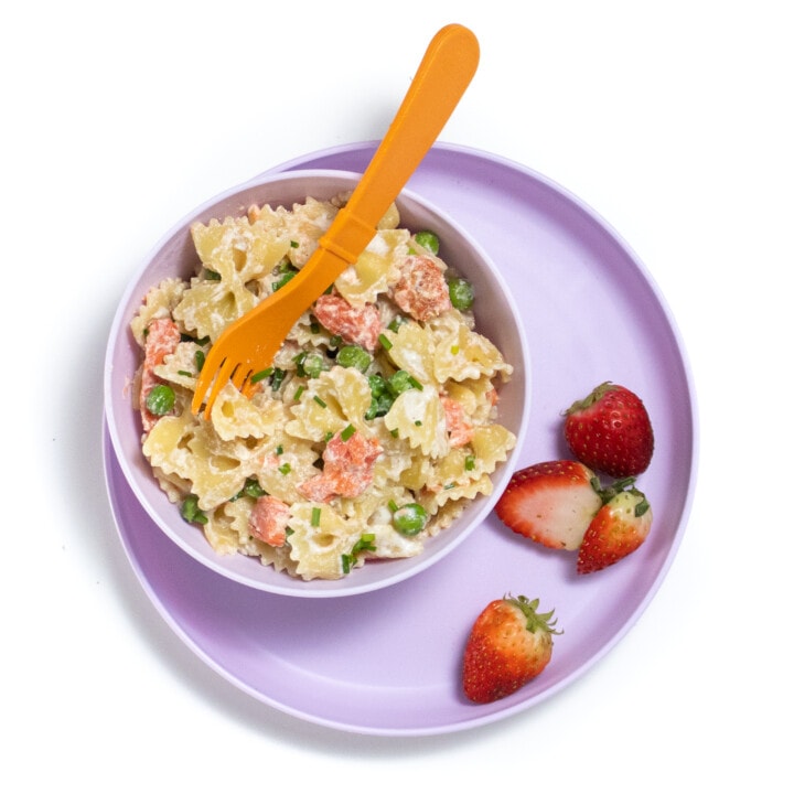 Kids purple plate filled with salmon pasta with peas and strawberries on the plate.