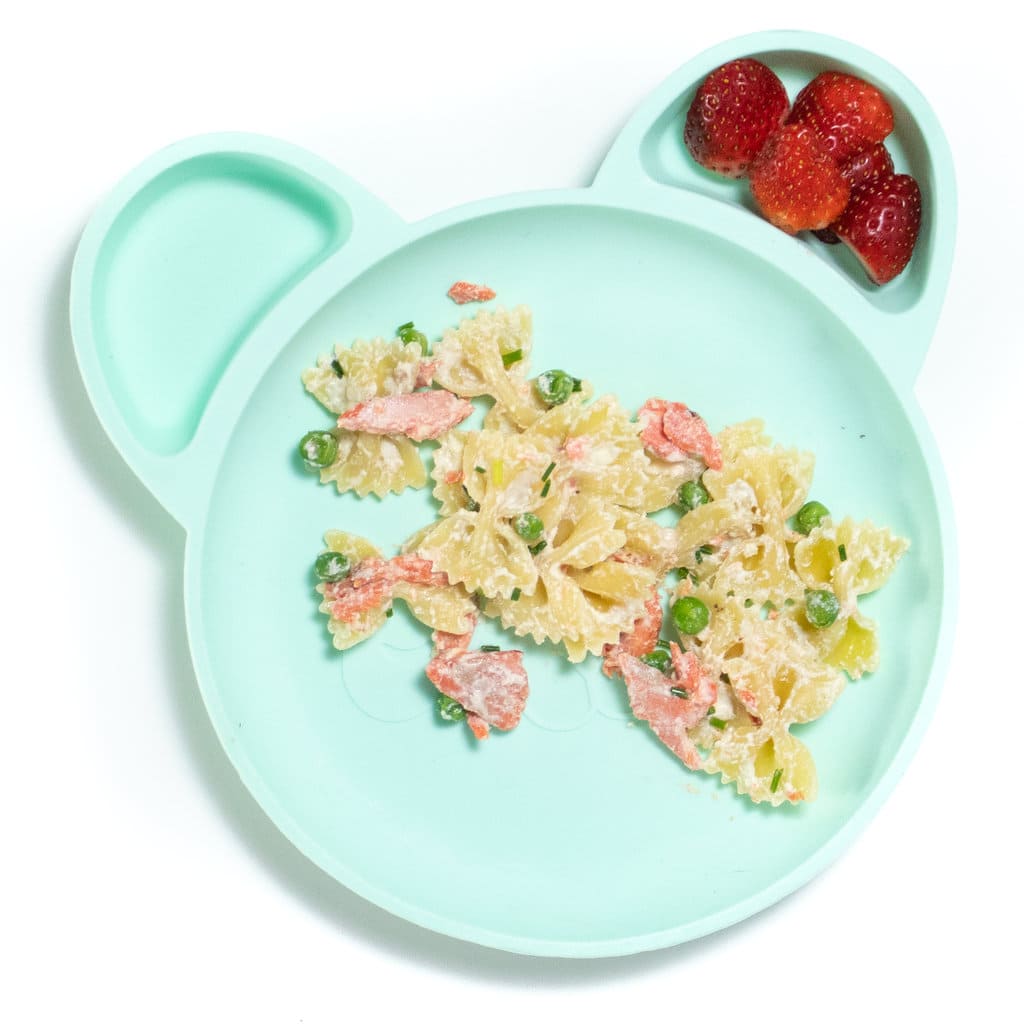 Baby plate full of salmon pasta and a side of strawberries.
