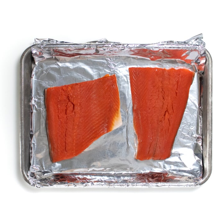 2 fillets of salmon sitting on a baking sheet covered in foil.