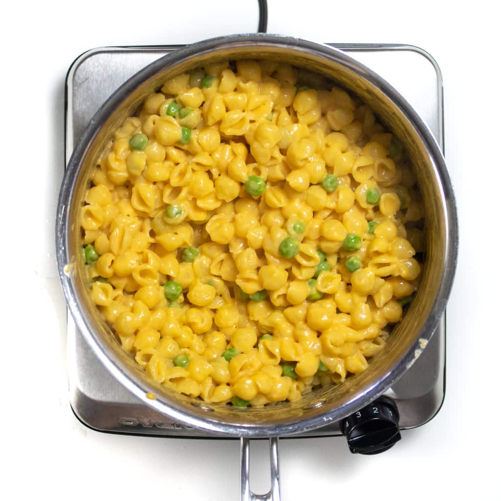 A silver sauce pan with sweet potato mac & cheese with peas in it
