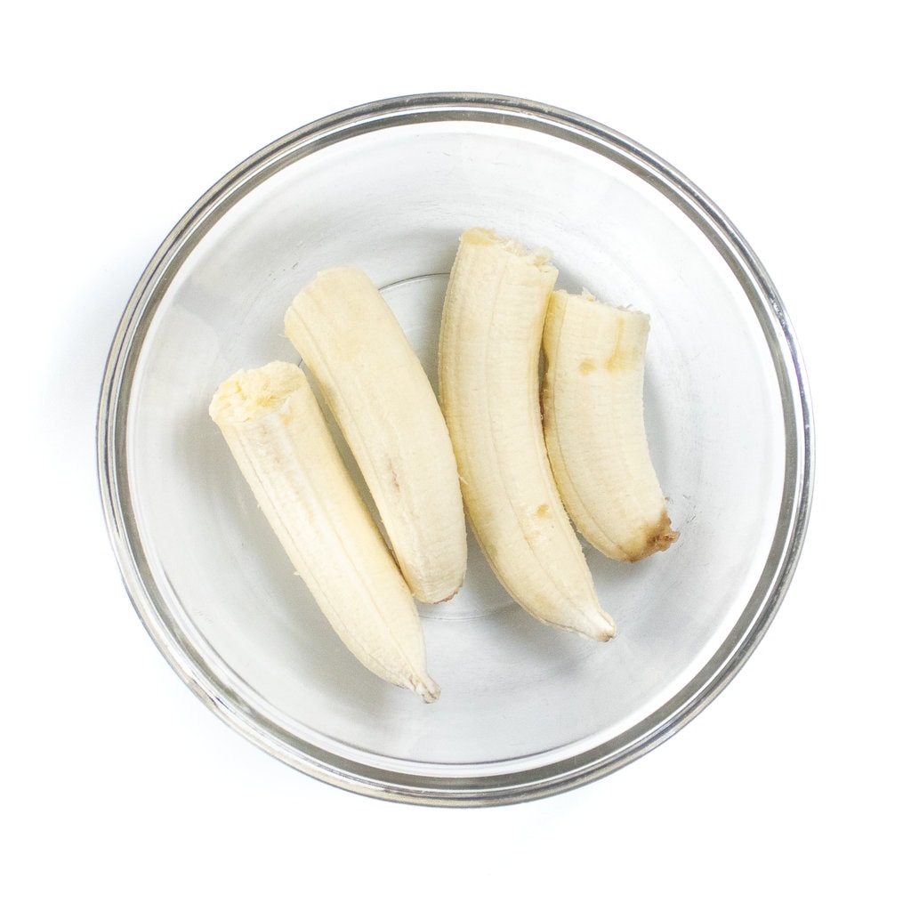 Clear glass bowl on a white background with two bananas cut enough.