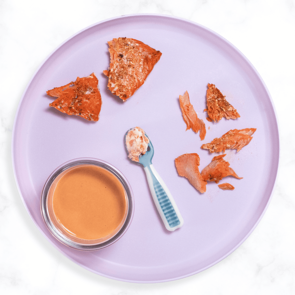 Purple baby plate sitting on my white kitchen counter with roasted salmon for baby.