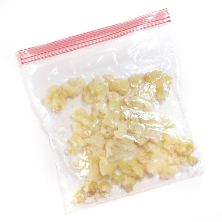 Plastic freezer bag filled with frozen cauliflower against a white backdrop.