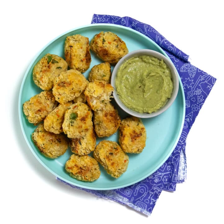 A teal kids plate full of cauliflower tots with a kids napkin against a white background.
