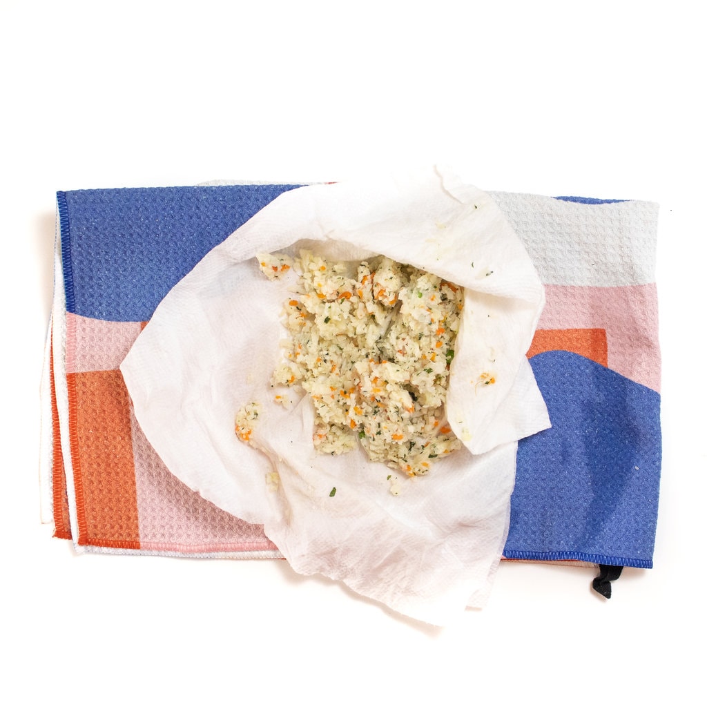 A white surface with a dish towel and a square of paper towel with cauliflower rice and vegetables.