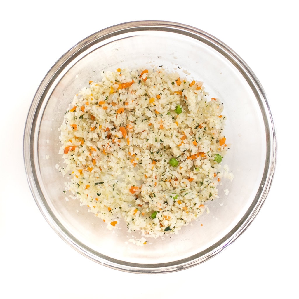 A clear glass bowl full of rice cauliflower and vegetables.